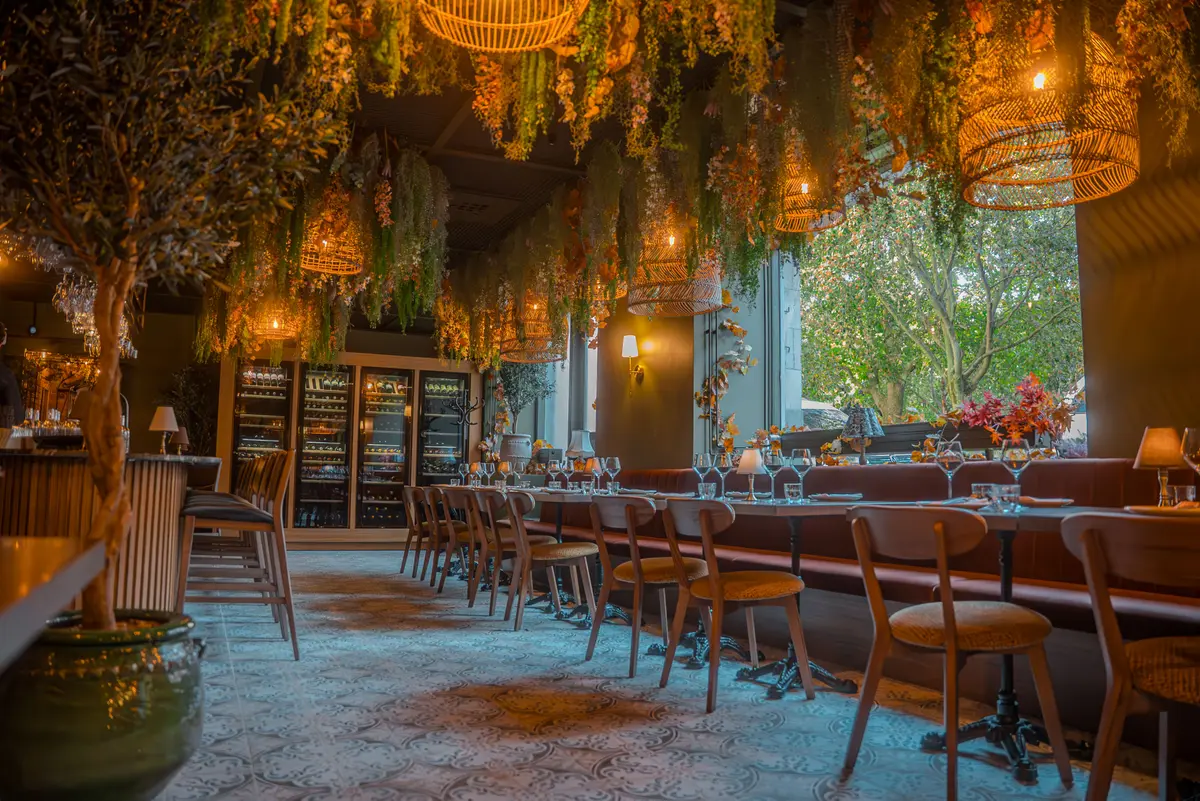 Matsal – långbord under tak av hängande blommor intill vinkylar på Tabbouli Skånegatan